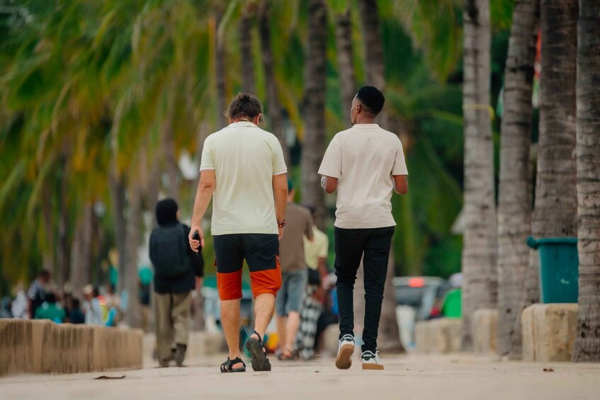 Two people walking on a beach with palm trees and parked cars in the background. 3