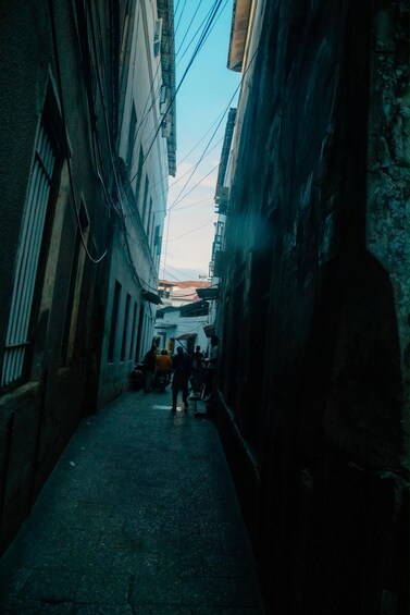 A narrow alleyway between buildings with visible electrical wires and a few people walking. 4