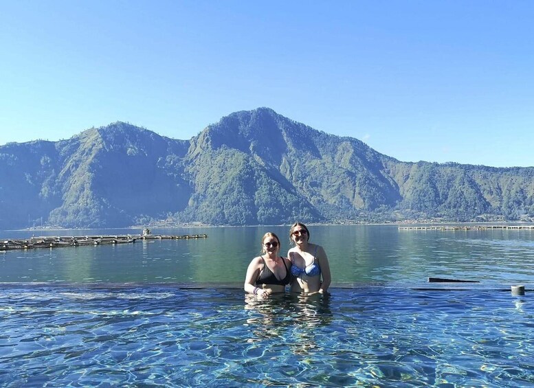 Two people in a clear blue pool with mountains in the background. 4