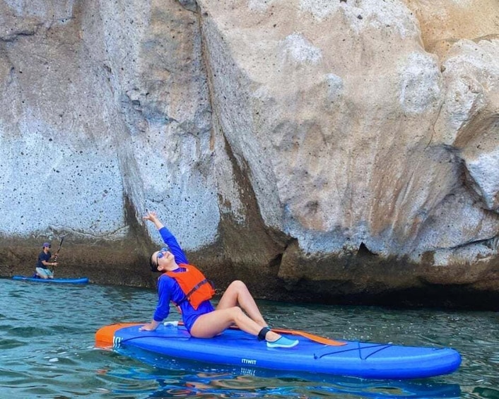 A person kayaking on a blue kayak with an orange life jacket, near a rocky cliff. 1