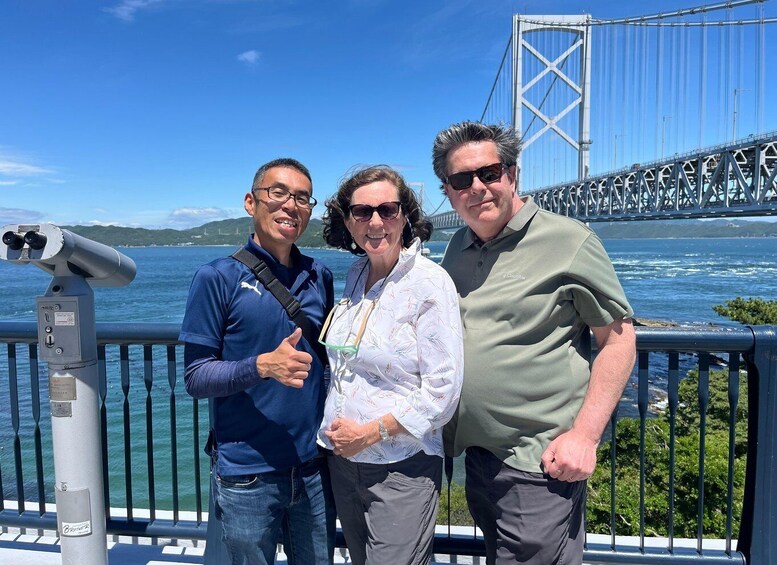 Three people standing by a railing with a bridge and water in the background. 2