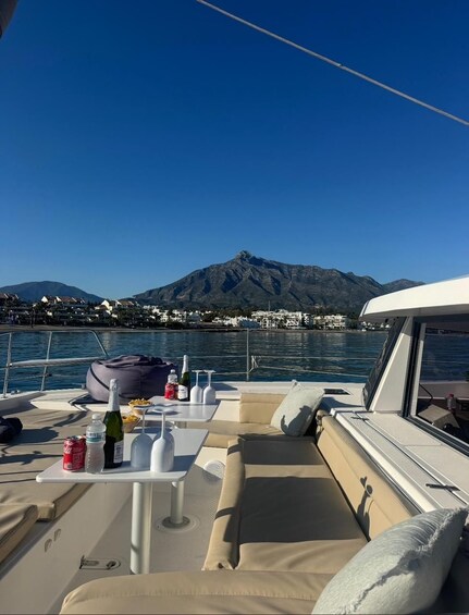 A boat deck with a table set for dining, a mountain in the background, and calm water. 3