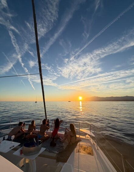 A sunset over a calm sea with a boat and people relaxing on the deck. 5