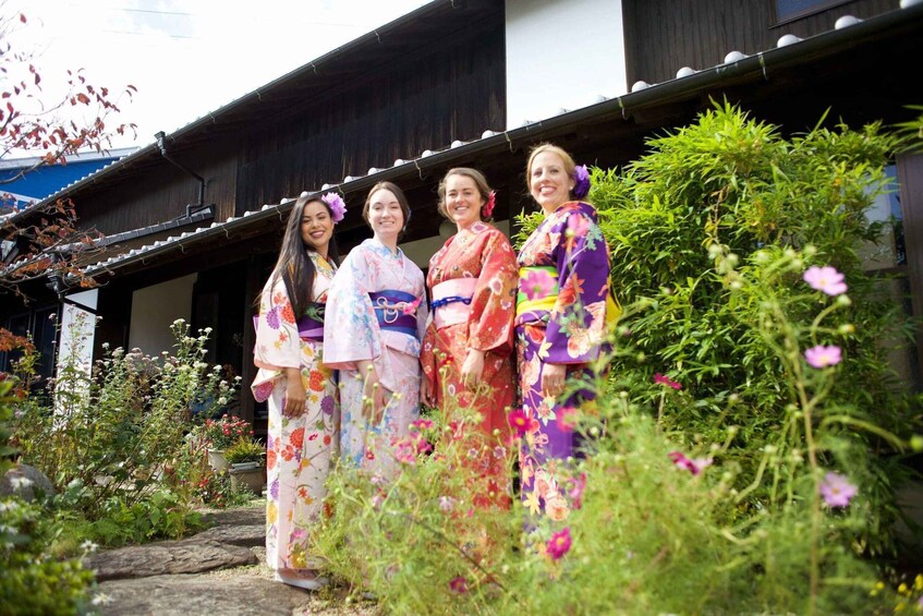 Four women in colorful kimonos standing in a garden with a traditional Japanese building in the background. 5