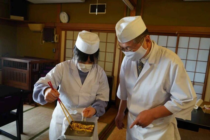 Two people in traditional attire preparing food in a room with tatami mats and a clock on the wall. 4