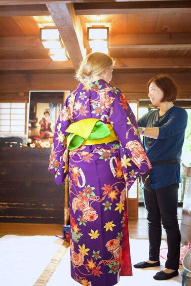 A person in a purple kimono with floral patterns standing indoors. 2