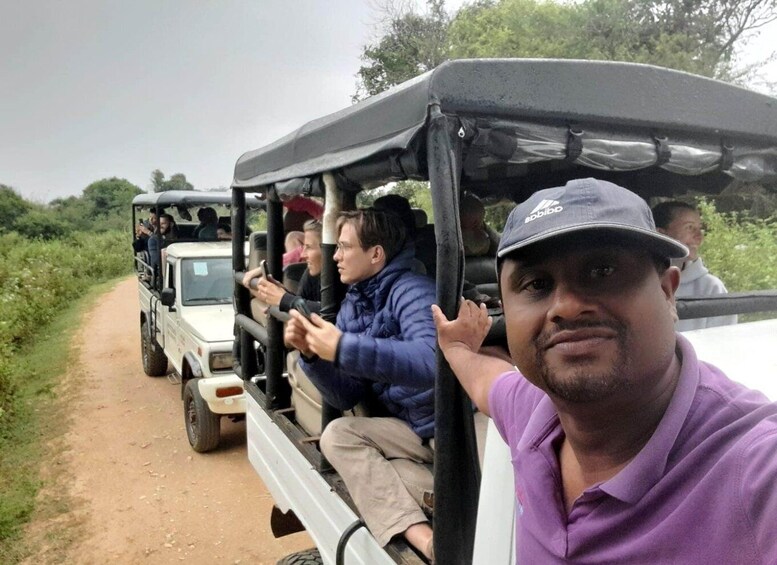 A group of people on a safari vehicle driving on a dirt road surrounded by greenery. 2