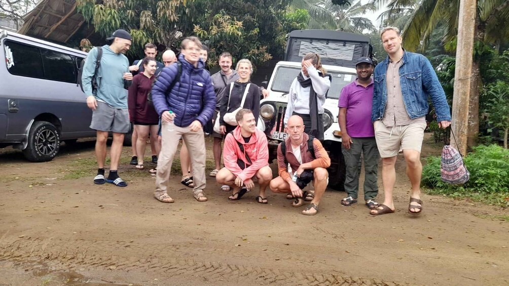 A group of people posing in front of a vehicle on a dirt road with tropical vegetation in the background. 4
