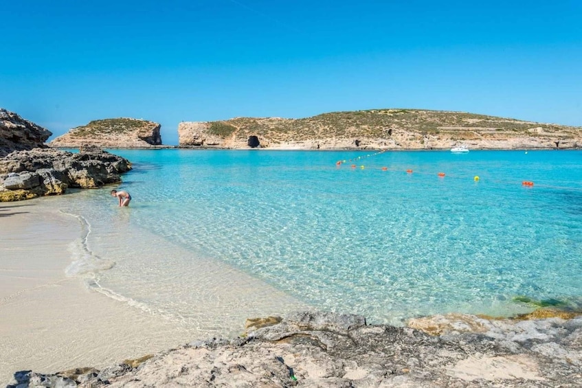 A clear blue sea with rocky shores, a sandy beach, and a boat in the distance. 3