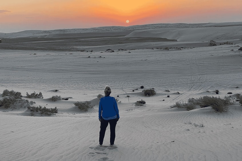 A person standing on a desert sand dune with a sunset in the background. 5