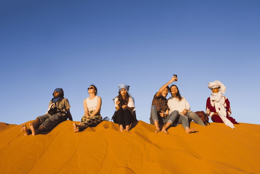 A group of people sitting on a sand dune. 1