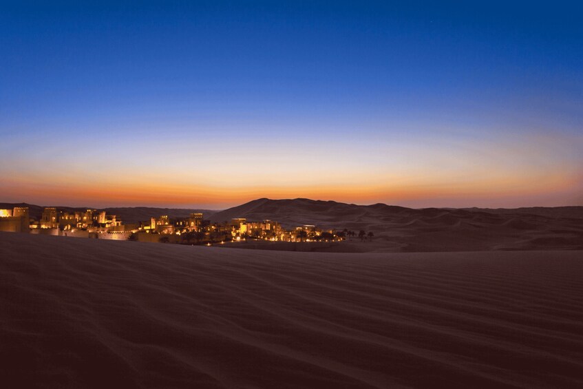 A desert landscape at dusk with a city illuminated in the distance. 2
