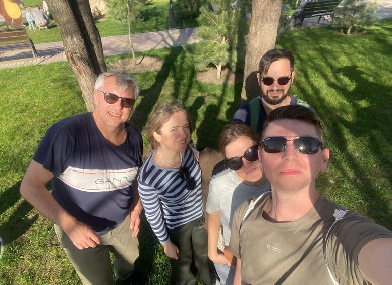 A group of people standing outdoors in a park with grass, trees, and a pathway. 4
