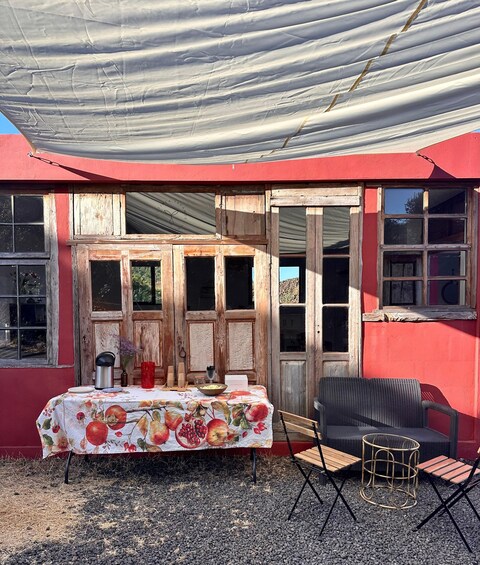 A rustic outdoor setting with a table covered in a floral tablecloth, a wicker chair, and a metal table. 3
