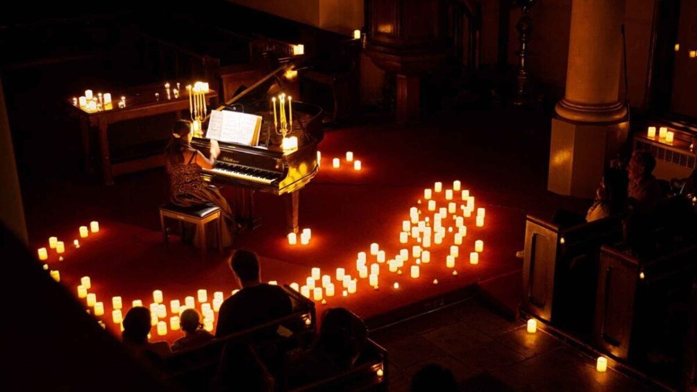 A grand piano on a stage with a crowd of people seated in front, surrounded by candles. 3