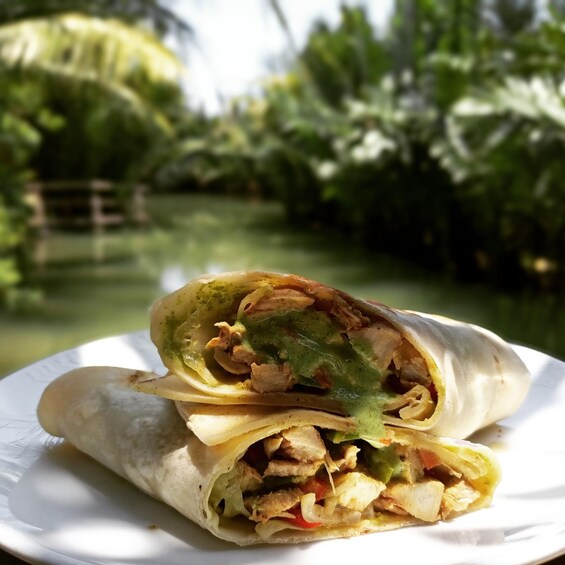 A burrito on a white plate with a blurred outdoor background. 2