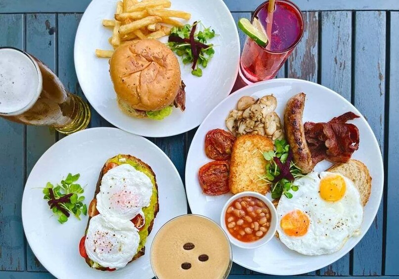 A meal with a burger, fries, eggs, bacon, beans, and a drink. 1
