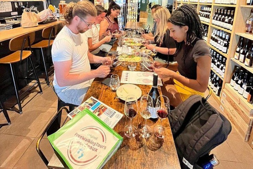 Un groupe de personnes déguste du vin dans un bar, avec des bouteilles de vin exposées sur des étagères derrière eux. 2