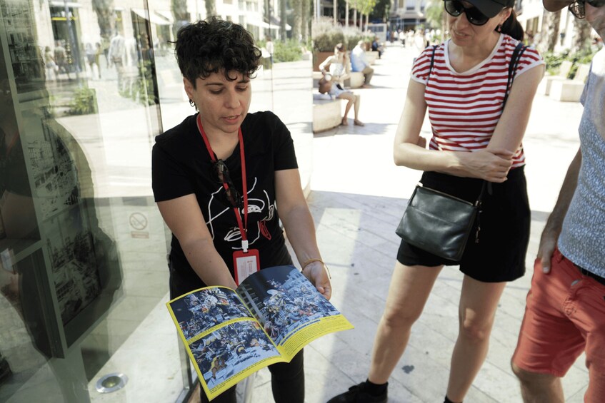 A person reading a magazine in an outdoor setting with glass walls and reflections of people. 5