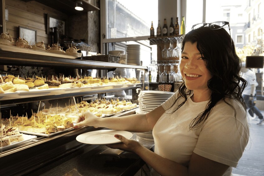 A person serving food from a buffet counter with various dishes and glasses. 1
