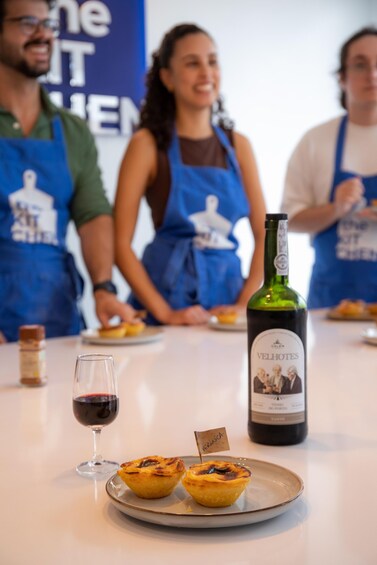 A group of people in aprons, a bottle of Vinho Verde wine, and two small pastries on a plate. 2