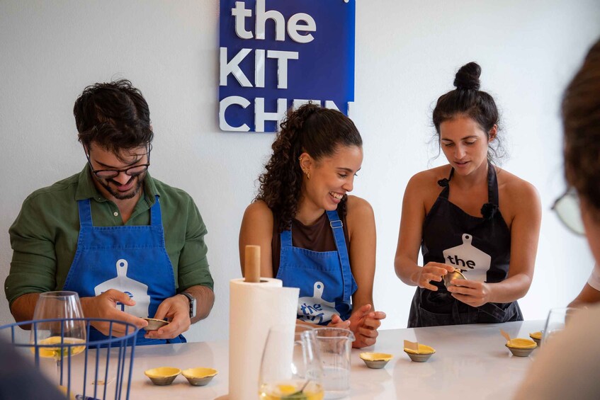 Three people in aprons at a table with cooking utensils and ingredients. 4