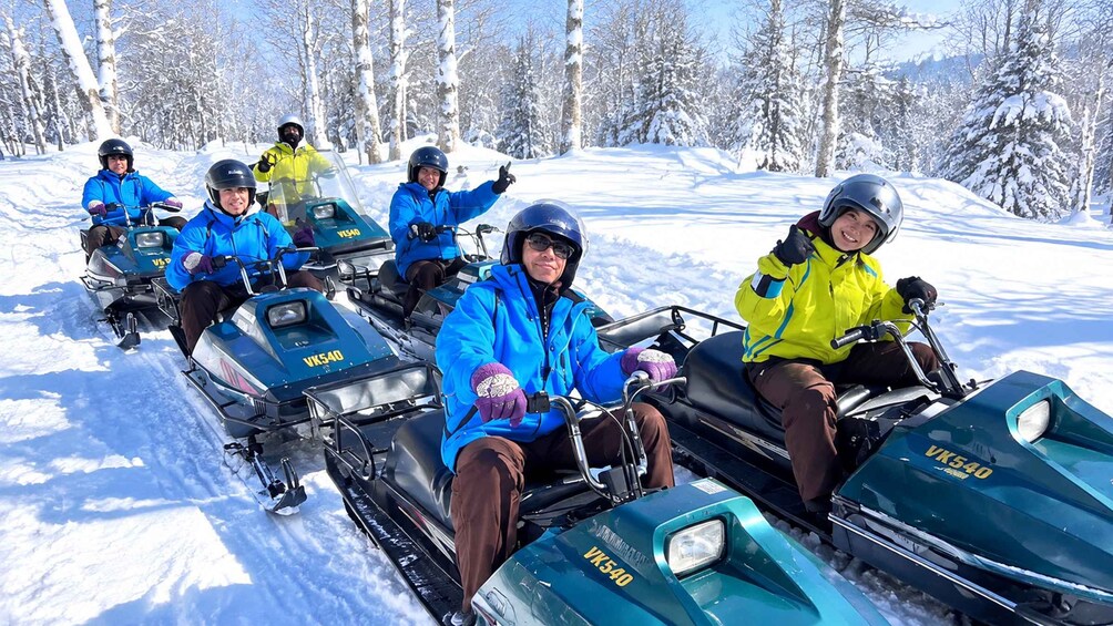 A group of people on snowmobiles in a snowy forest. 1