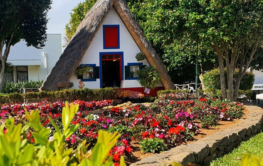 A thatched-roof house with a red door and blue trim, surrounded by a colorful flower garden. 1