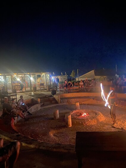A nighttime outdoor gathering with a fire pit and people sitting around. 5