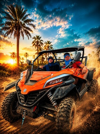 Two people in an orange off-road vehicle on a dirt path with palm trees and a sunset in the background. 1
