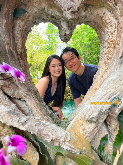 Two people inside a heart-shaped rock formation with a waterfall and greenery in the background. 5