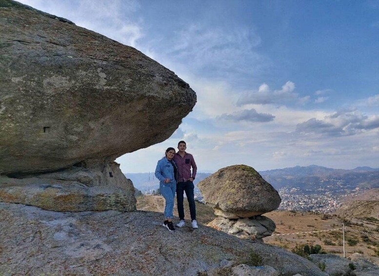 Two people standing under a rock formation with a view of a distant town. 3
