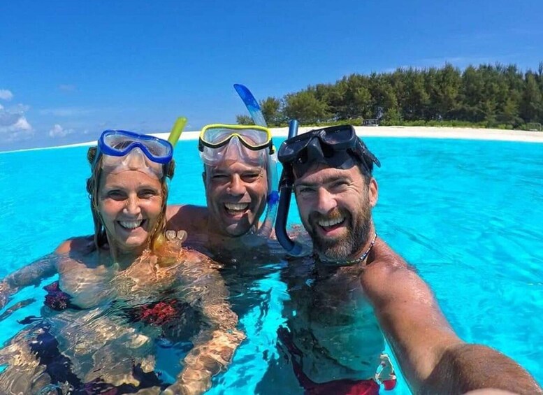 Tre persone fanno snorkeling in acque cristalline, con un'isola ricoperta da vegetazione sullo sfondo. 1