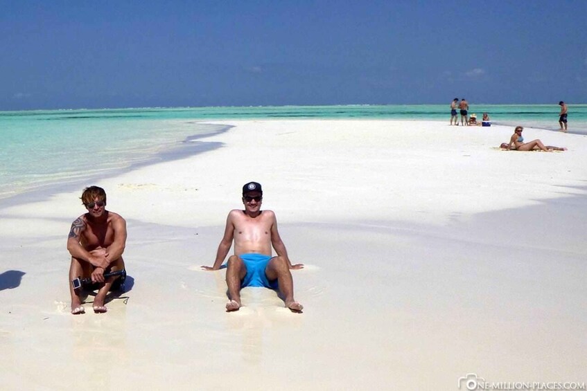 Due persone sedute su una spiaggia di sabbia bianca con acque turchesi sullo sfondo. 5