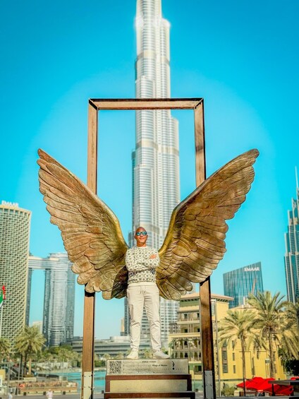 A statue of a man with wings in front of a tall skyscraper. 5