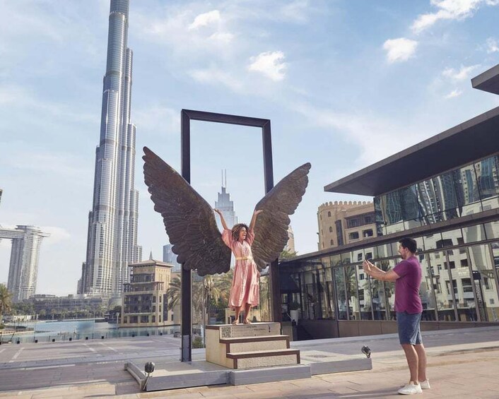 A statue of an angel with outstretched wings in an urban setting with modern buildings and a tall skyscraper in the background. 1