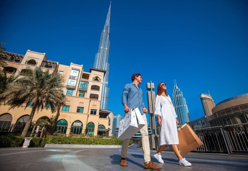 A couple walking in a plaza with palm trees and modern buildings, including a tall skyscraper. 4