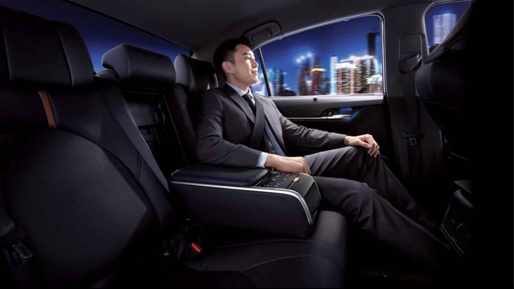 A man in a suit sitting in a luxurious car with a cityscape visible through the window. 1