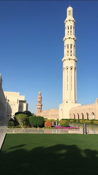 A tall minaret with a clock tower in the background, surrounded by greenery and a body of water. 4