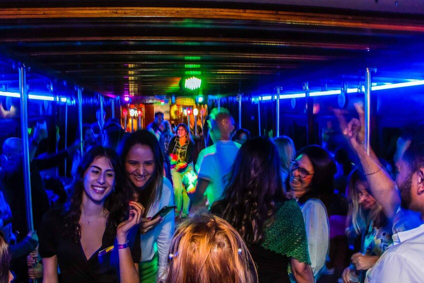 A crowded indoor space with people standing and socializing, illuminated by colorful lights. 3