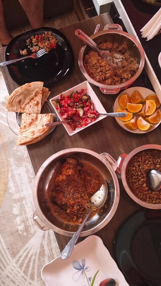 A table with various dishes including rice, a vegetable salad, orange slices, flatbread, and a meat dish. 4
