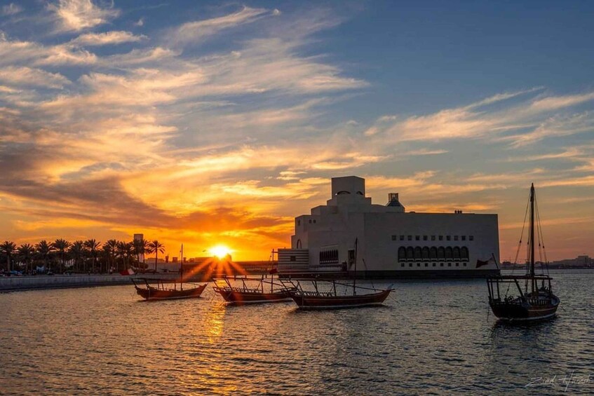 A sunset over a body of water with traditional boats and a modern building. 2