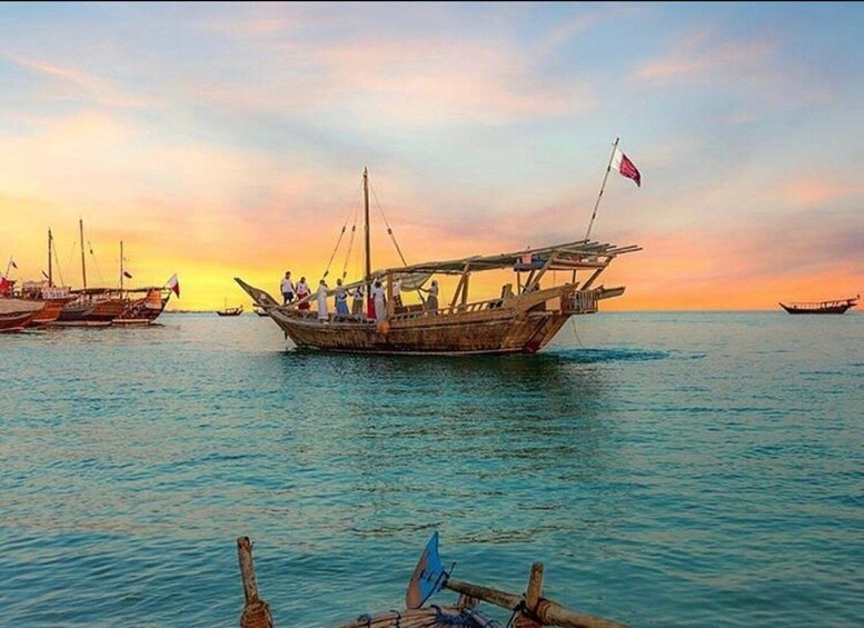 A traditional wooden boat with people on it, sailing on calm waters during sunset. 5