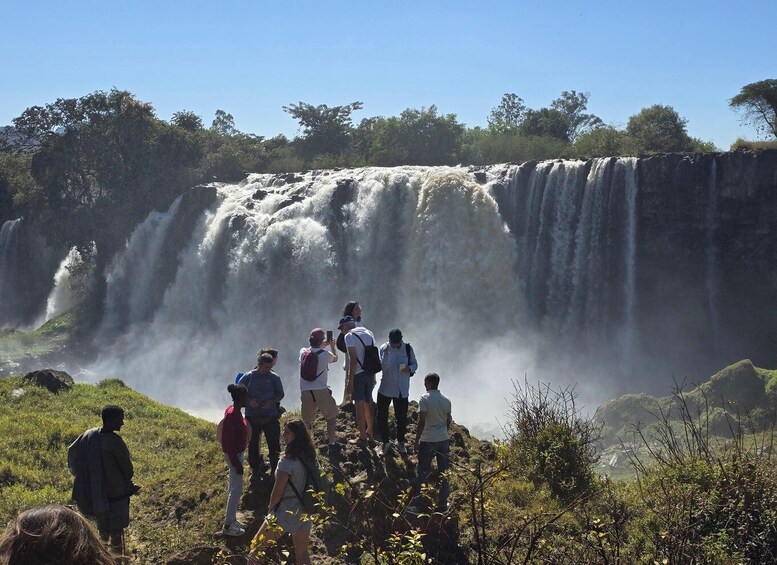 A group of people standing on a hill overlooking a large waterfall. 1