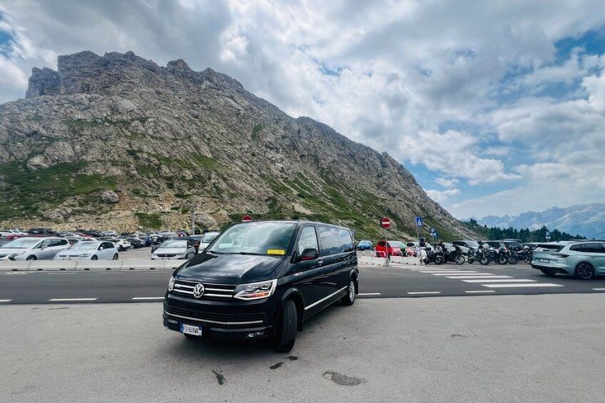 A parking lot with a black van in the foreground, a mountain range in the background, and several parked cars. 4