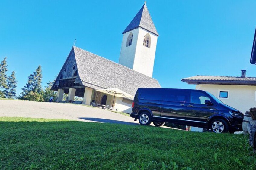 A church with a bell tower, a van parked in front, and a grassy area. 3