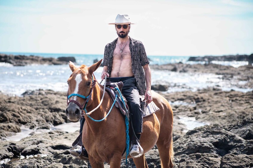 A person riding a horse on a rocky beach with the ocean in the background. 4