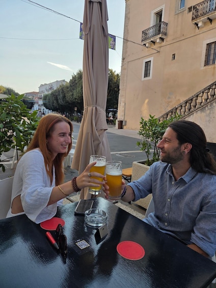 Two people toasting with beer glasses at an outdoor table with a QR code and a red coaster. 5