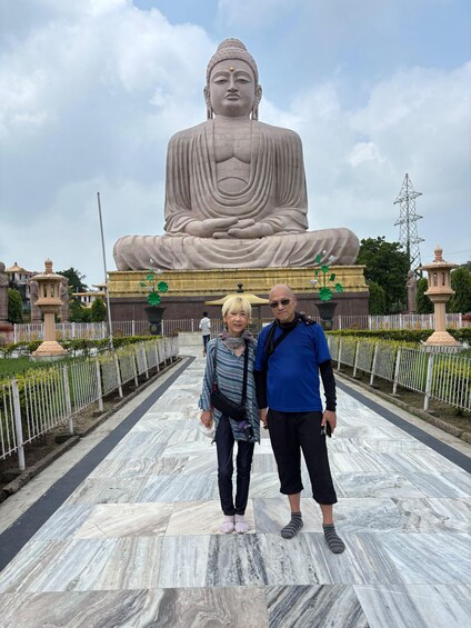Two people standing in front of a large Buddha statue. 1