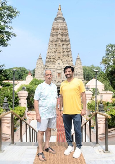 Two people standing in front of a large, ornate temple with a tall spire. 4